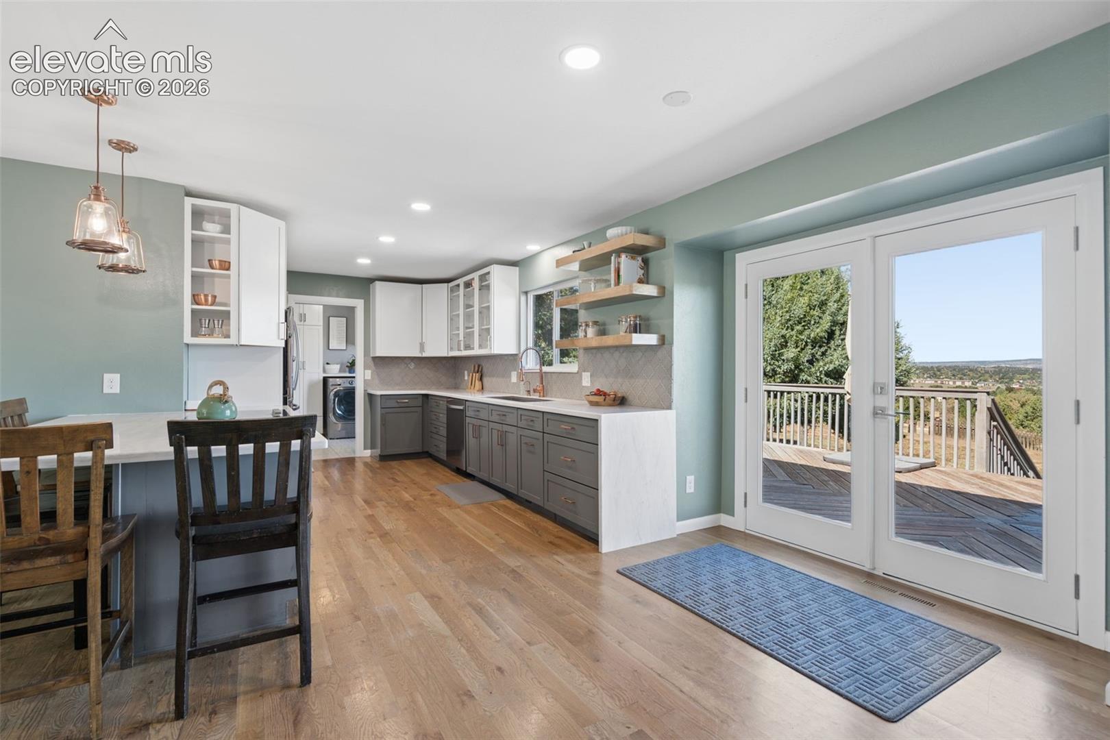 Kitchen featuring shaker-style cabinetry, stone countertops, wood-finish flooring, floating wood shelving, and dual French doors