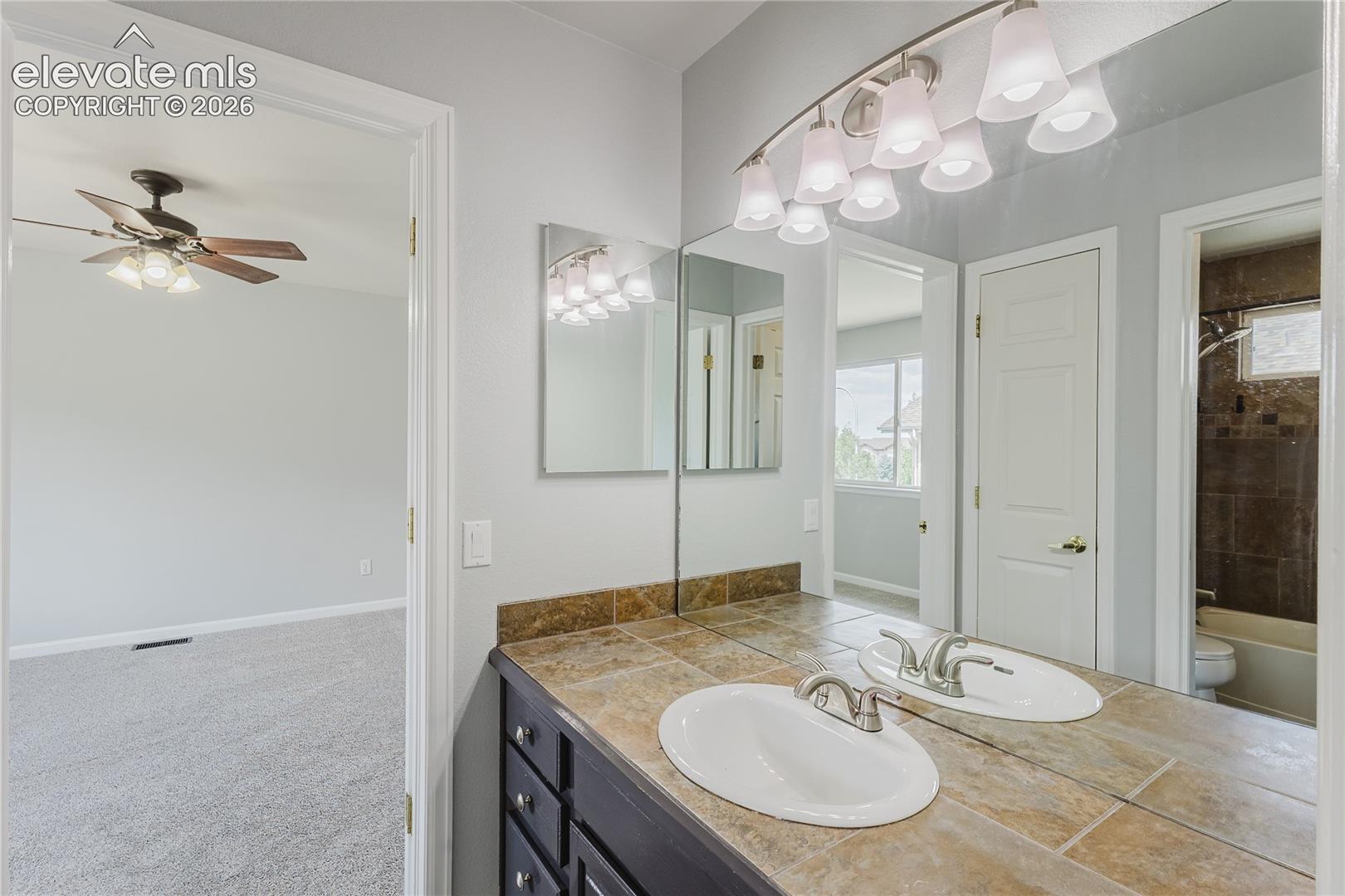 Double vanity with integrated sinks and brushed nickel faucets, tile countertop, and expansive wall-mounted mirror