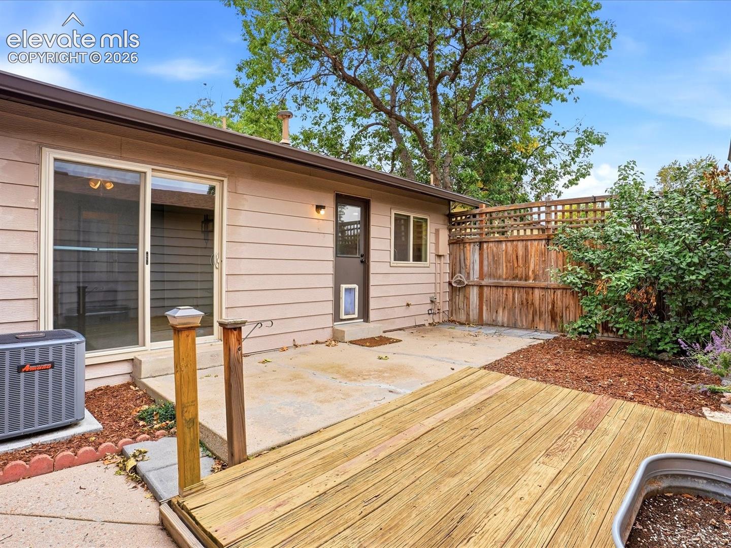Rear exterior featuring a wood deck, concrete patio, wood privacy fencing, and sliding glass door