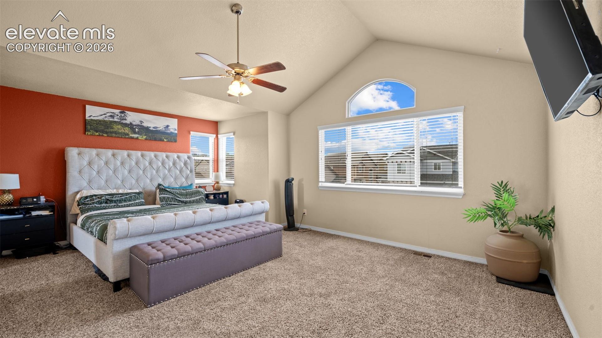Vaulted ceiling with an arched window, ceiling fan, and carpeted flooring