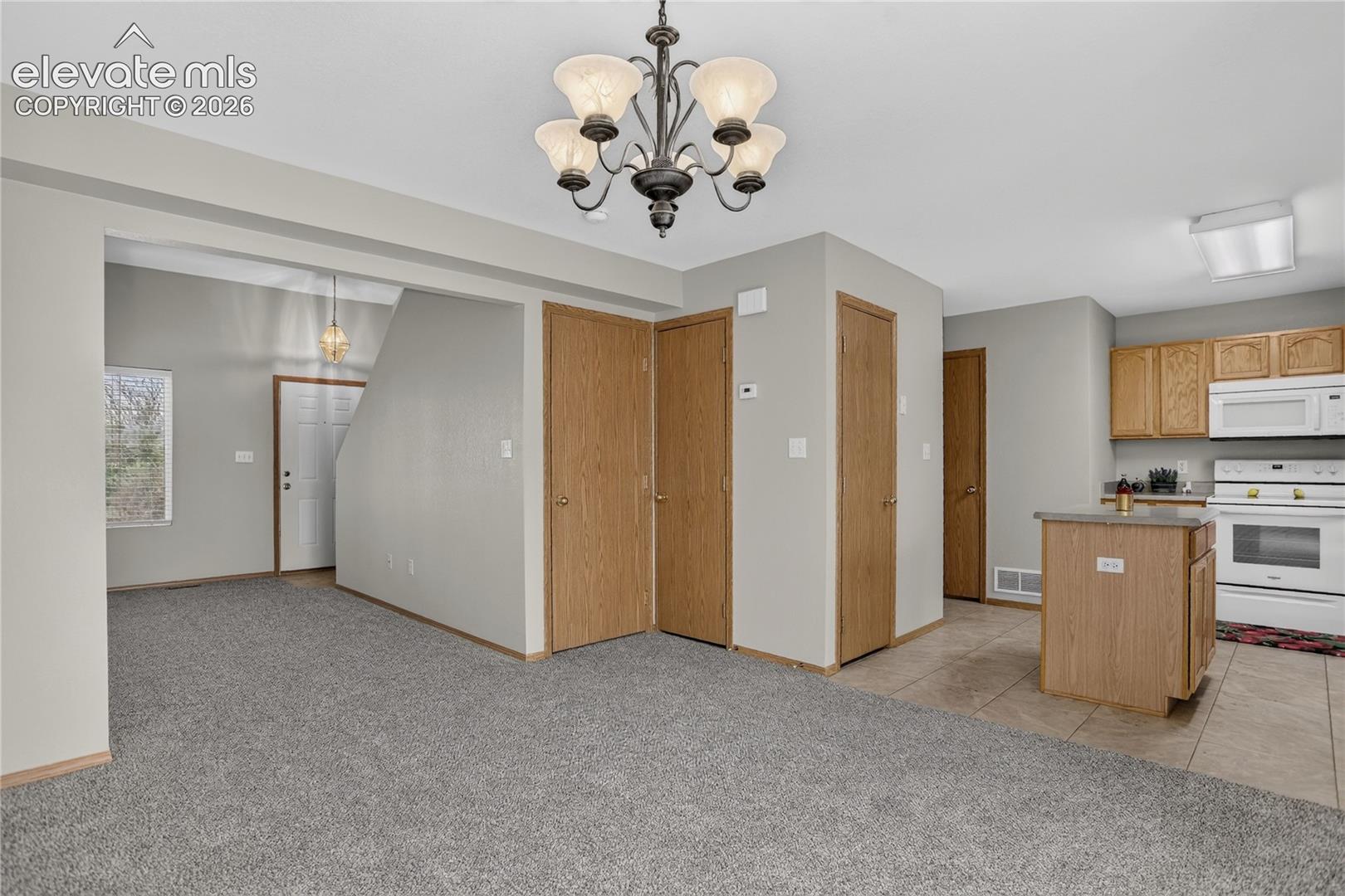 Open living area with neutral gray wall paint, carpeting, and a chandelier