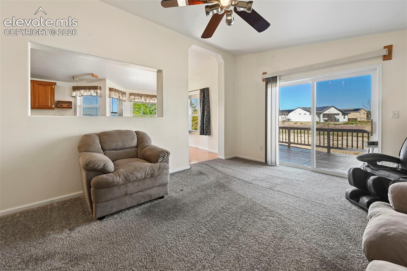 Interior featuring neutral wall-to-wall carpeting, ceiling fan with integrated lighting, pass-through wall opening, and sliding glass doors with access to an exterior deck