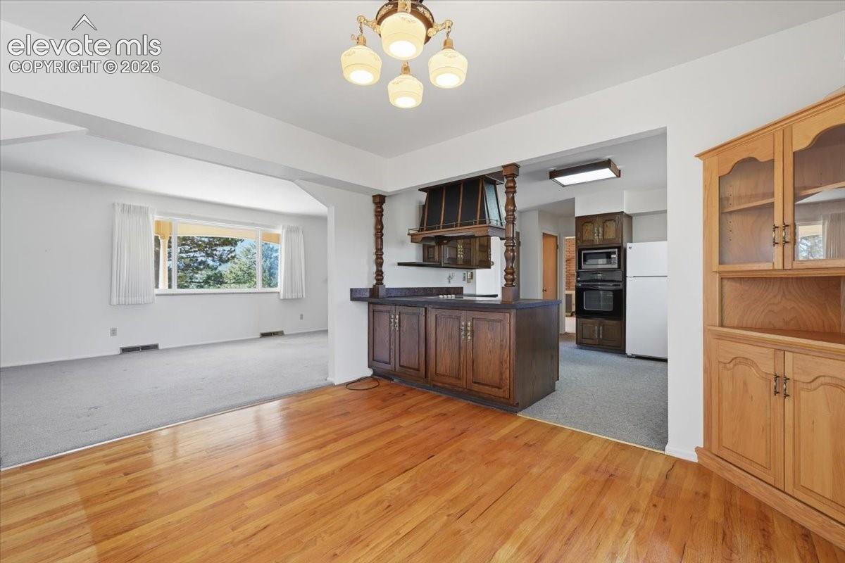 Hardwood flooring, kitchen island with built-in cabinetry, decorative wood-turned columns, built-in hutch, and integrated wall oven