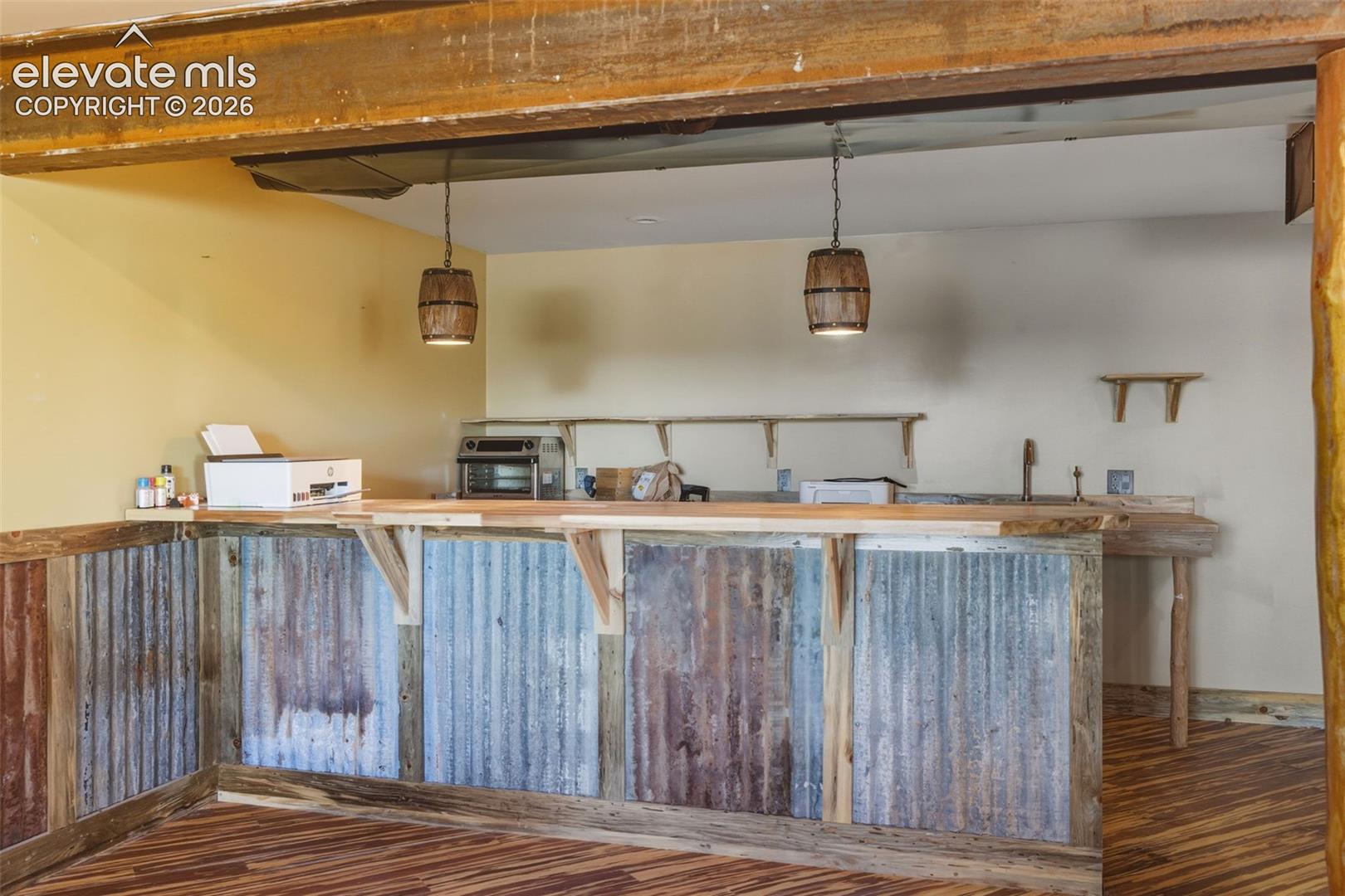 Bar area featuring corrugated metal and wood paneling, wood-finish flooring, two barrel-style pendant lights, and a built-in sink with a gooseneck faucet