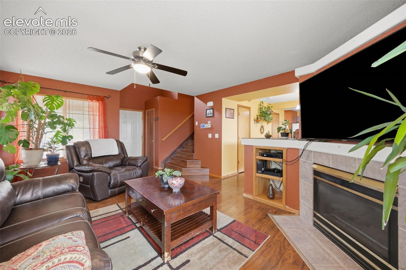 Living area featuring wood-finish flooring, a ceiling fan with integrated lighting, and a tiled fireplace