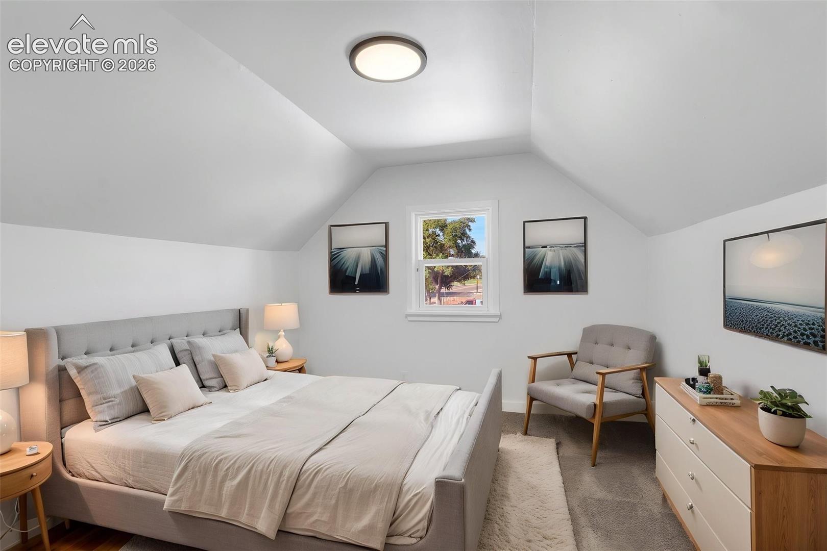 Room featuring vaulted ceilings, neutral wall tones, carpeted flooring, and a central flush-mount light fixture