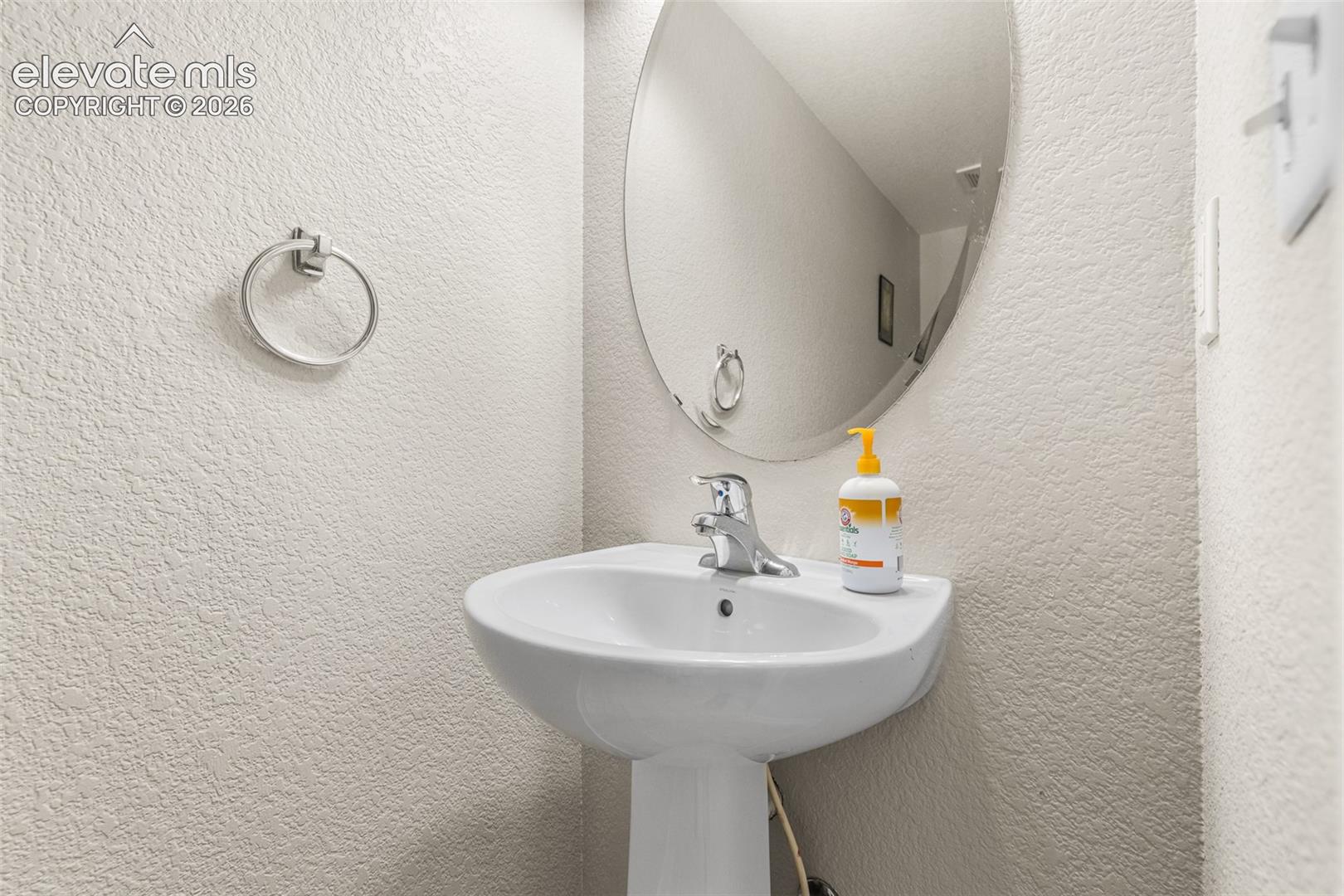 White pedestal sink with a chrome faucet, oval wall-mounted mirror, and circular metal towel ring