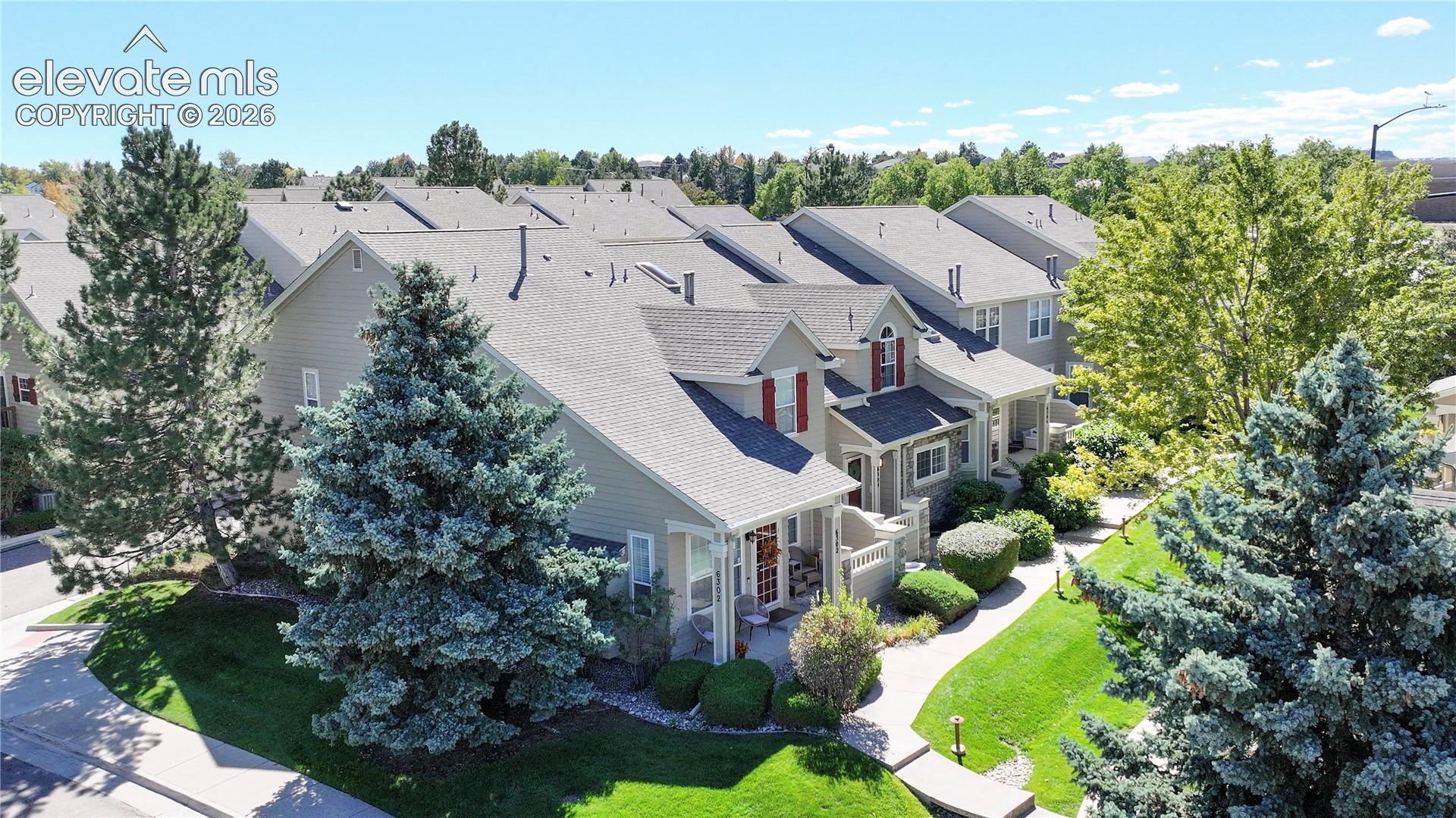 Multi-level townhome exterior featuring horizontal lap siding, a pitched shingle roof, decorative shutters, and stone veneer accents, complemented by mature evergreen landscaping