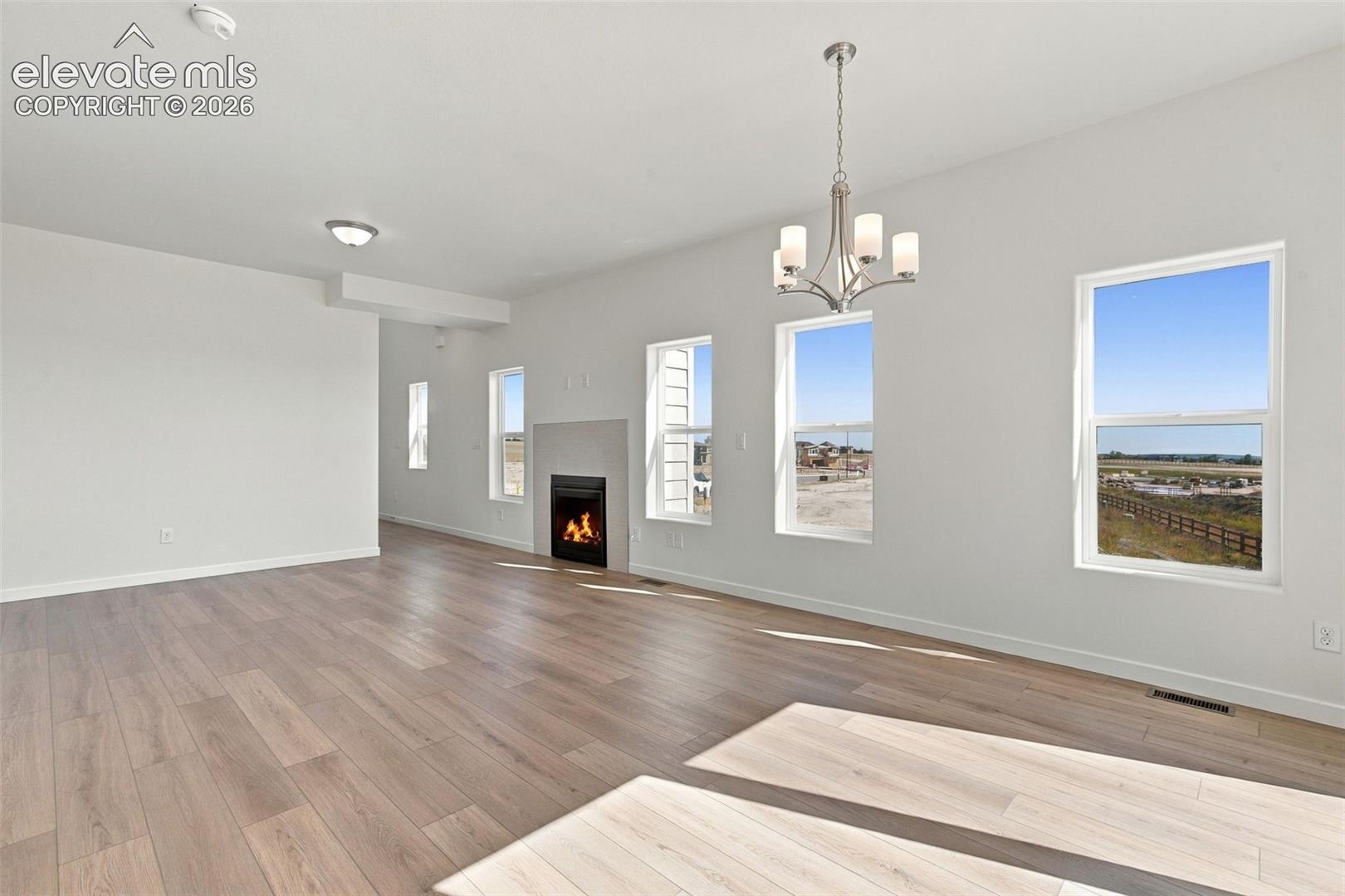 Open-concept living area with wood-finish flooring, a modern fireplace, multiple windows, and a decorative chandelier