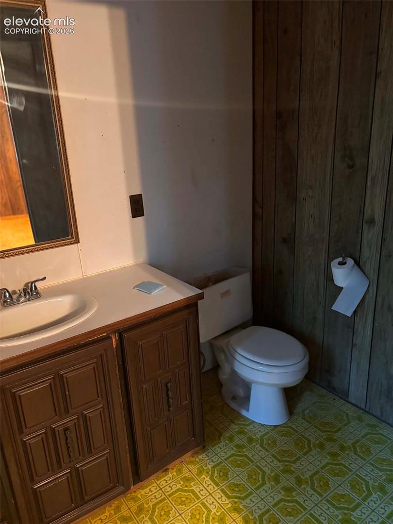 Bathroom featuring a vanity with wood-finish cabinetry, a white countertop, an integrated sink, and patterned resilient flooring with wood-paneled walls