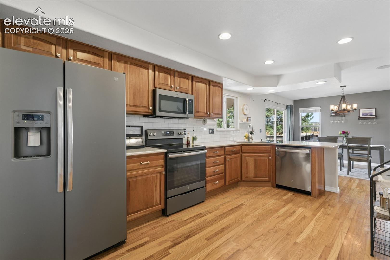 Kitchen featuring wood cabinetry, stainless steel appliances, white subway tile backsplash, and wood-finish flooring