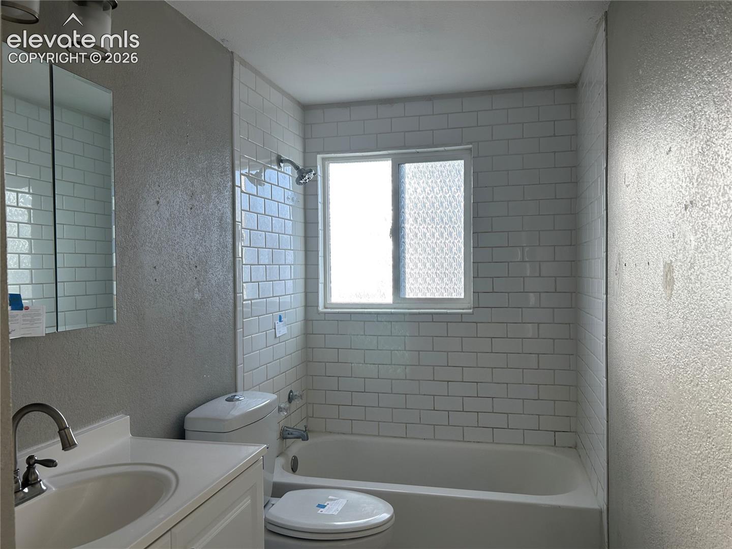 Bathroom featuring a white subway tile shower surround, a sliding glass window, a white vanity with an integrated sink, a wall-mounted medicine cabinet, and a polished chrome faucet