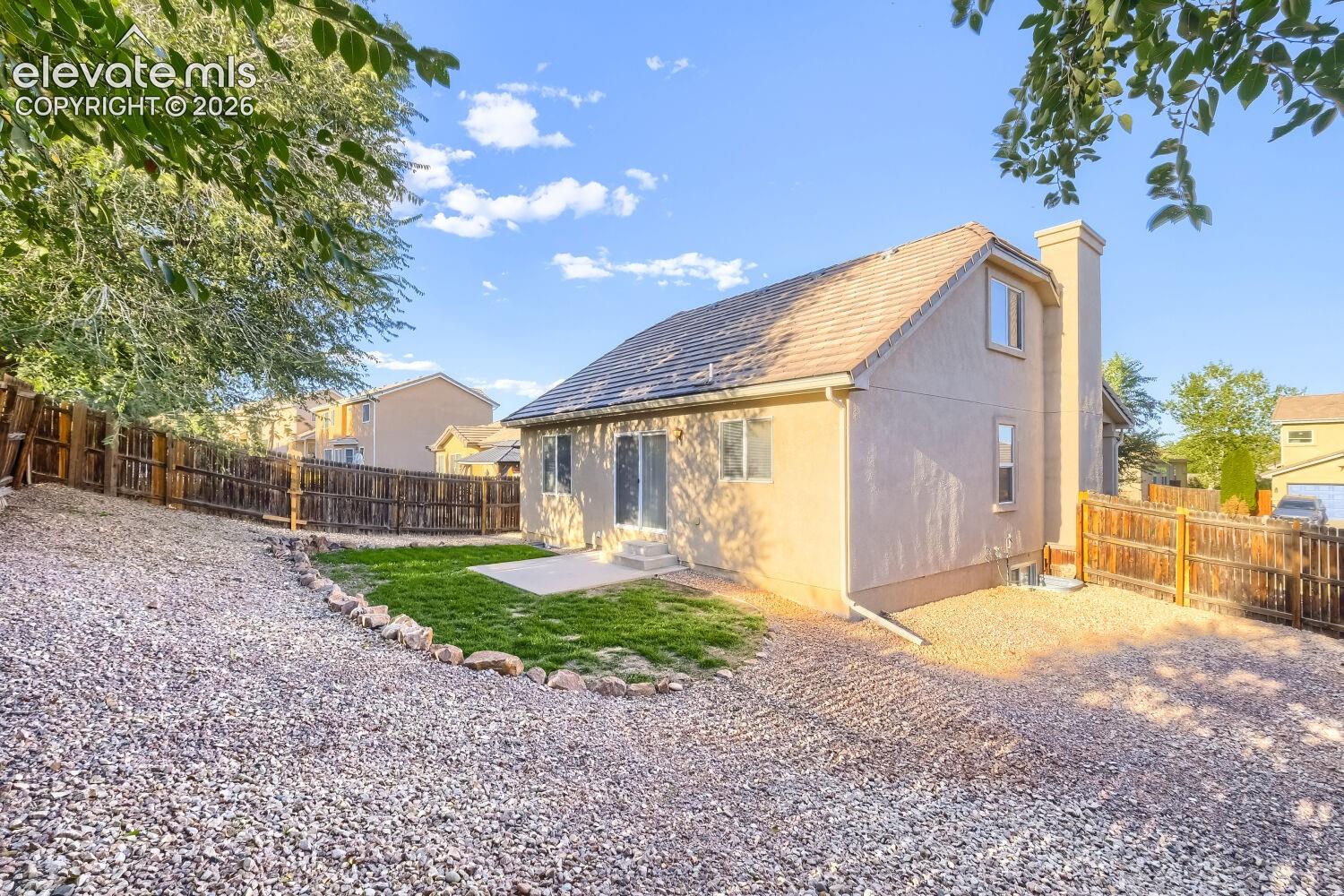 Rear exterior featuring a stucco facade, exterior chimney, concrete patio, grass lawn, and wood privacy fencing