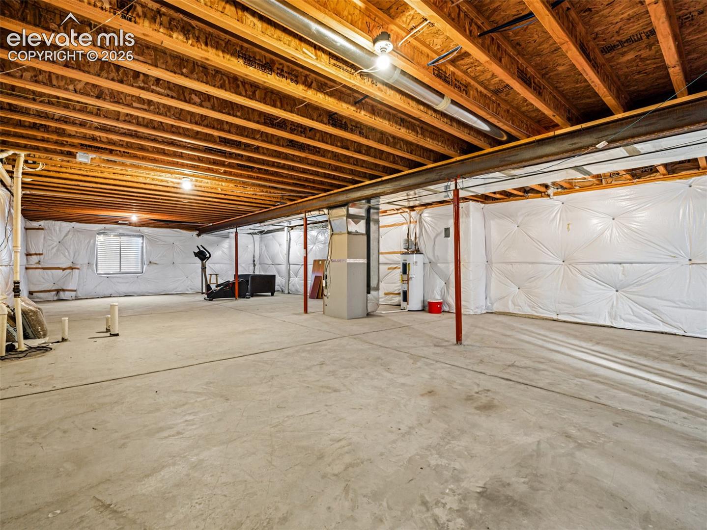 Unfinished lower level with concrete flooring, exposed wood joists, utility sink, and installed water heater