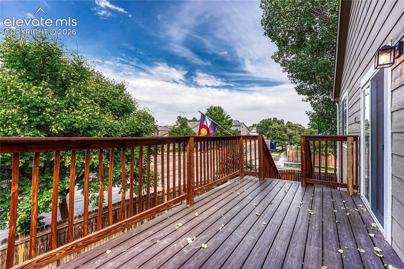 Elevated exterior deck featuring dark-toned plank flooring, wooden railing, and a wall-mounted outdoor light fixture