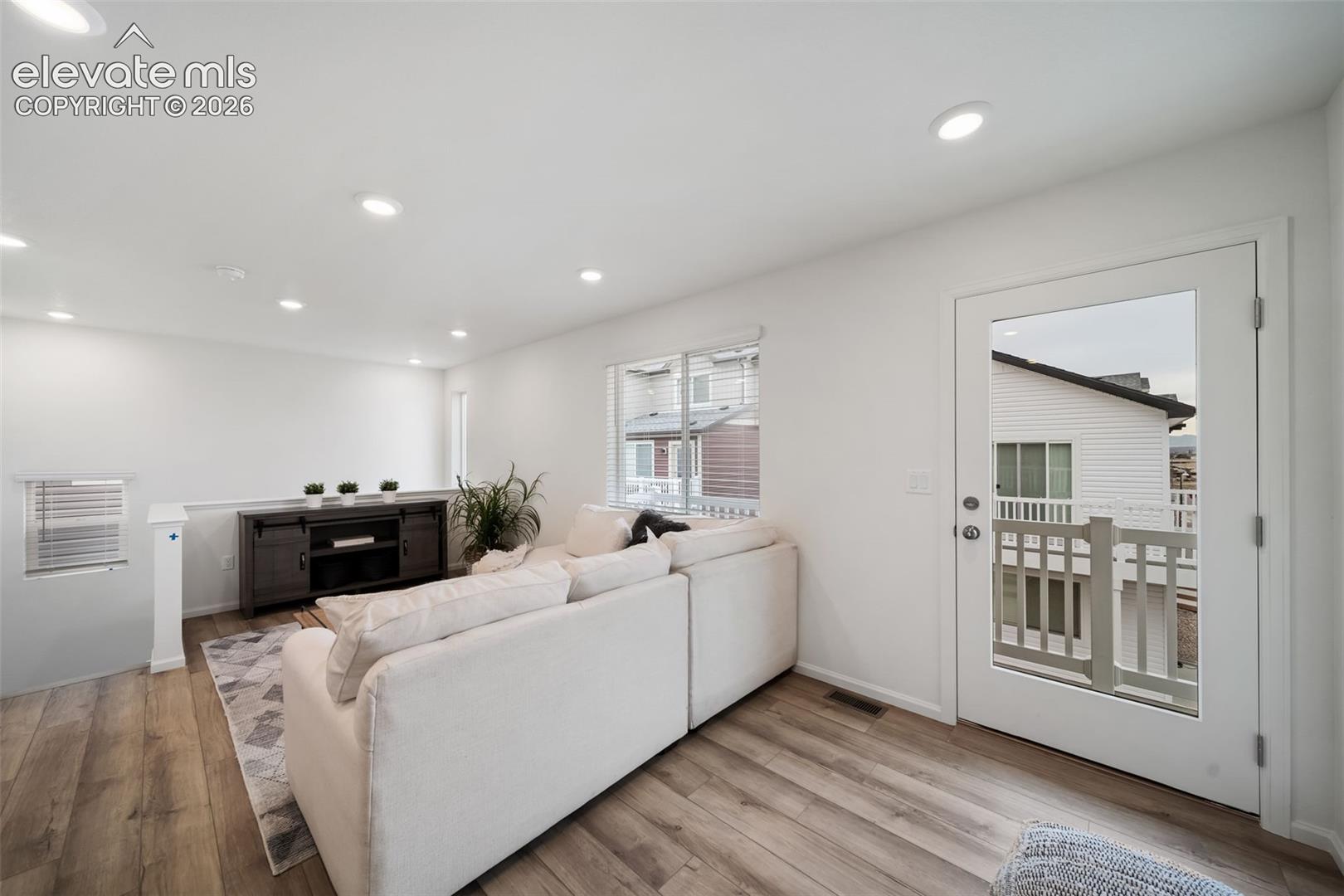 Recessed lighting, wood-finish flooring, white walls, and a glass-paneled door leading to an outdoor balcony