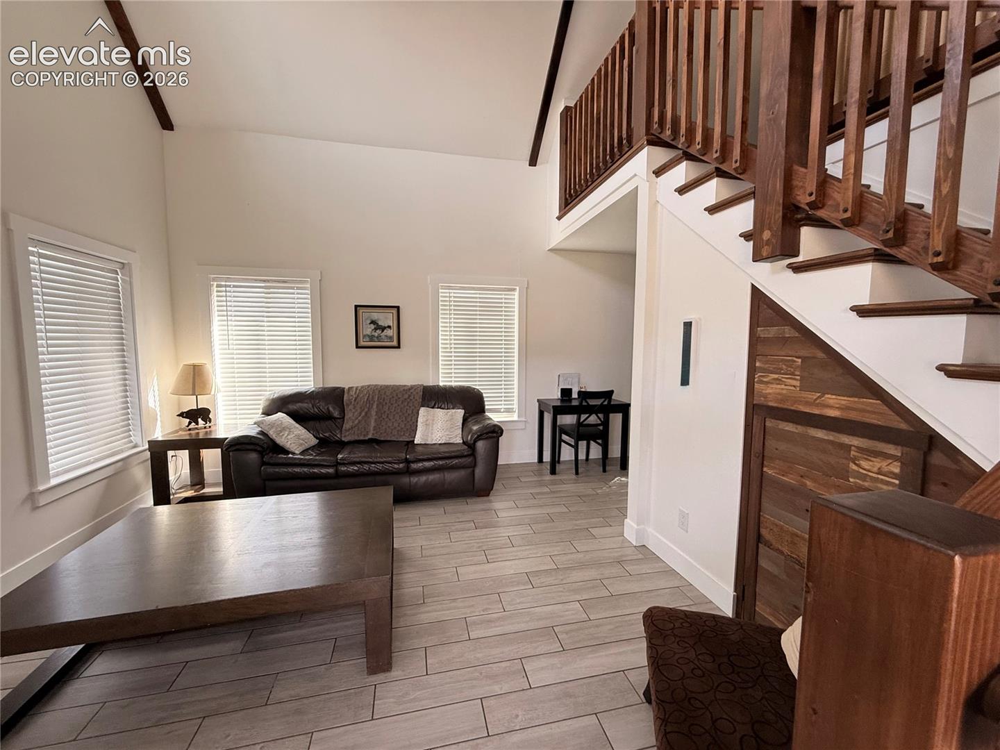 Vaulted ceiling, open wood staircase with balusters, wood-finish flooring, multiple windows, and a built-in wood-paneled storage feature under the staircase
