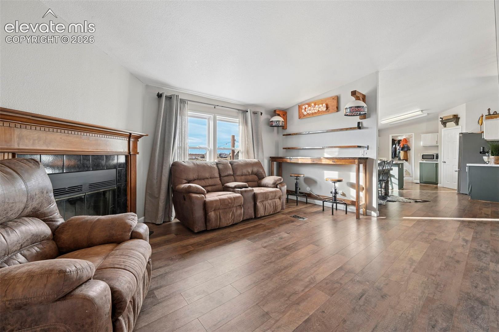Wood-finish flooring, fireplace with a decorative wooden mantel and tile surround, and custom built-in wooden bar shelving with integrated lighting