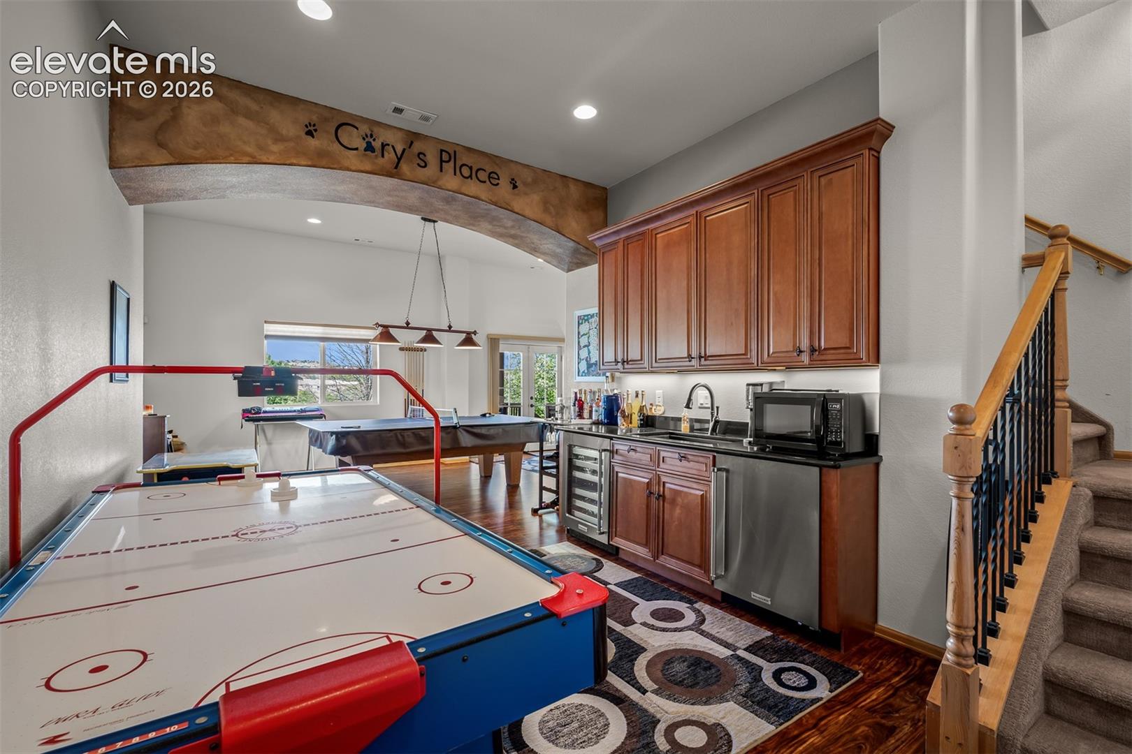 Entertainment room featuring a wet bar with wood cabinetry, dark countertops, wine cooler and mini-fridge on lower level.