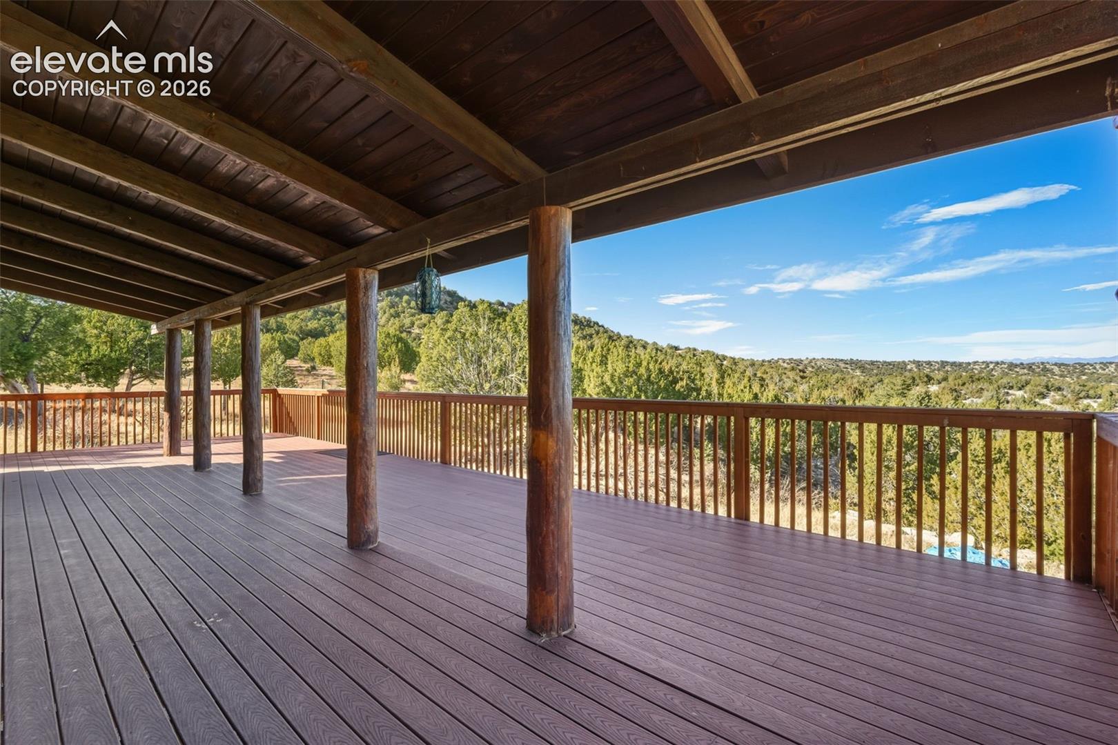 Expansive covered deck featuring wood-finish decking, substantial log columns, and wood railings