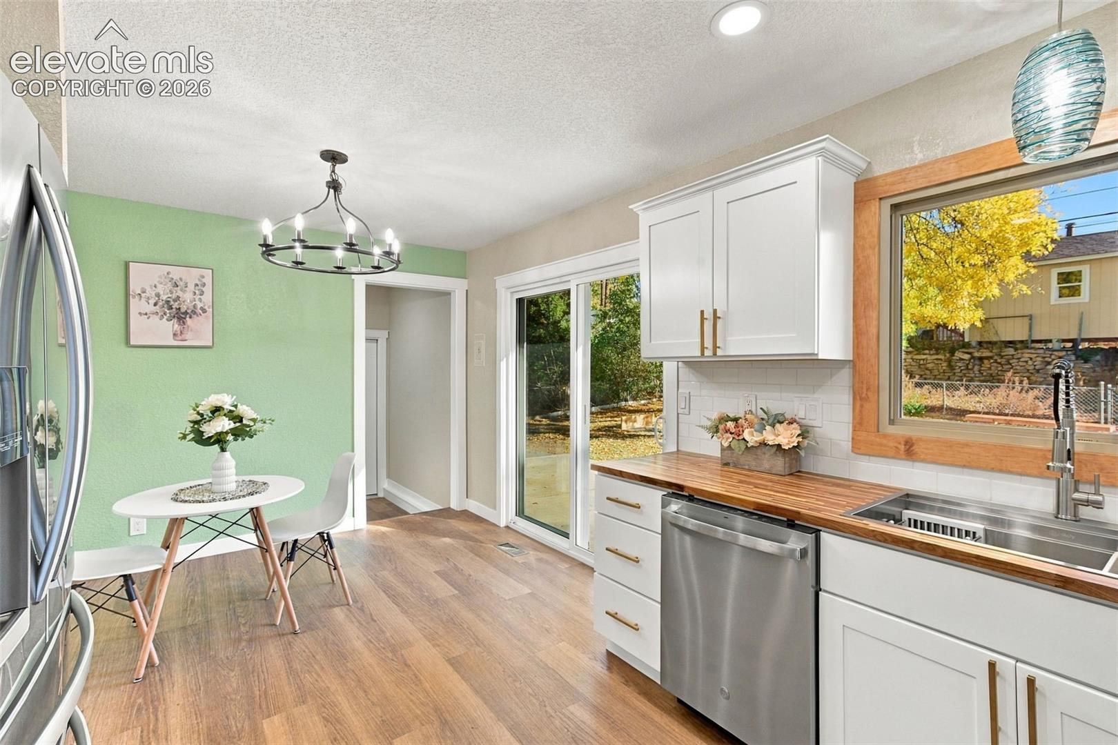 Kitchen featuring white shaker-style cabinetry, wood-finish countertops, stainless steel appliances, sliding glass doors, and wood-finish flooring