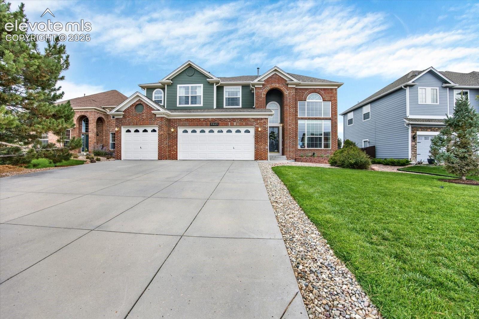 Two-story brick and siding facade featuring an arched entryway, multi-paned windows, and an attached three-car garage with a concrete driveway