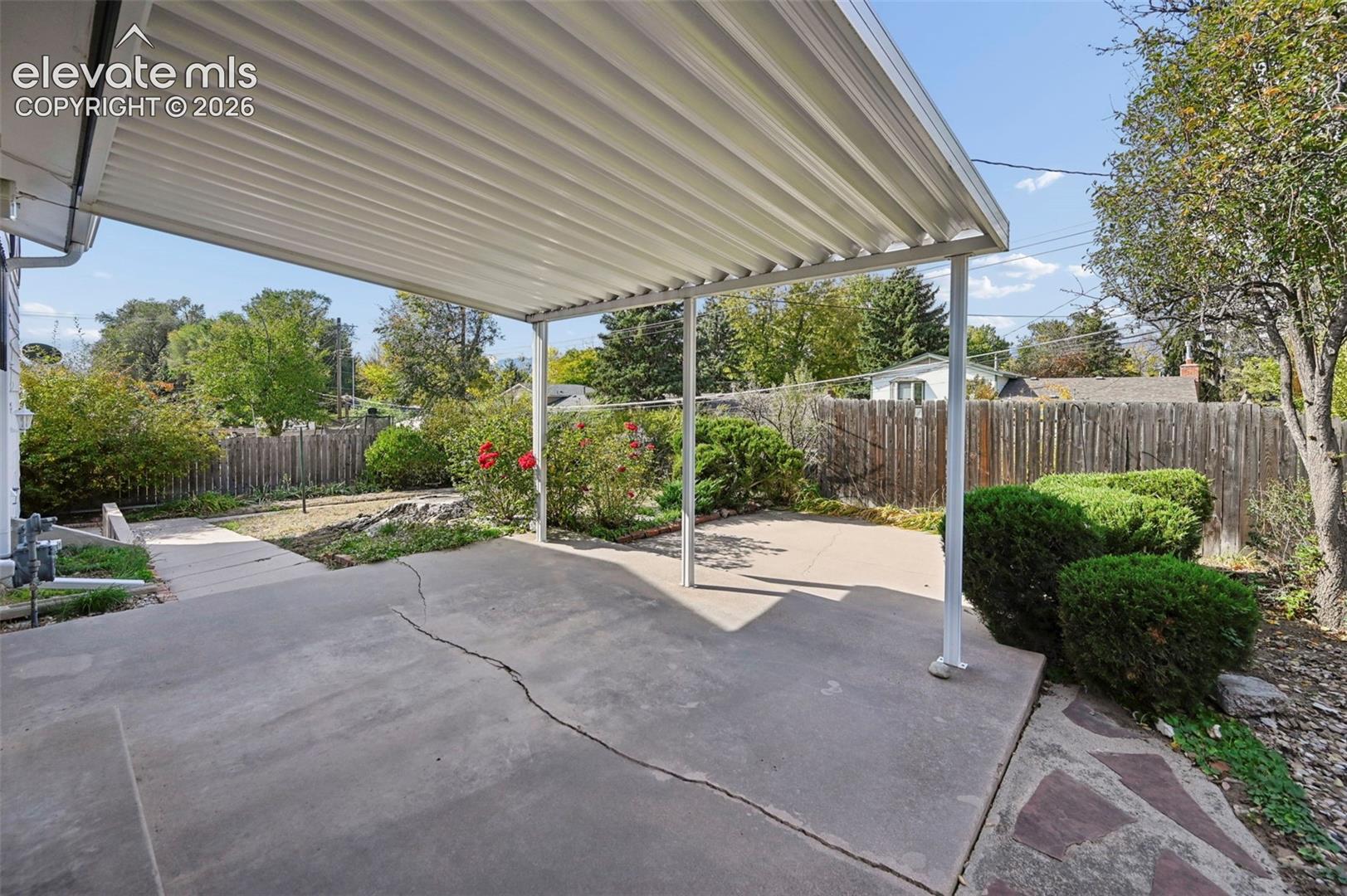 Covered patio overlooks back yard with mature landscaping, and private wood fence  