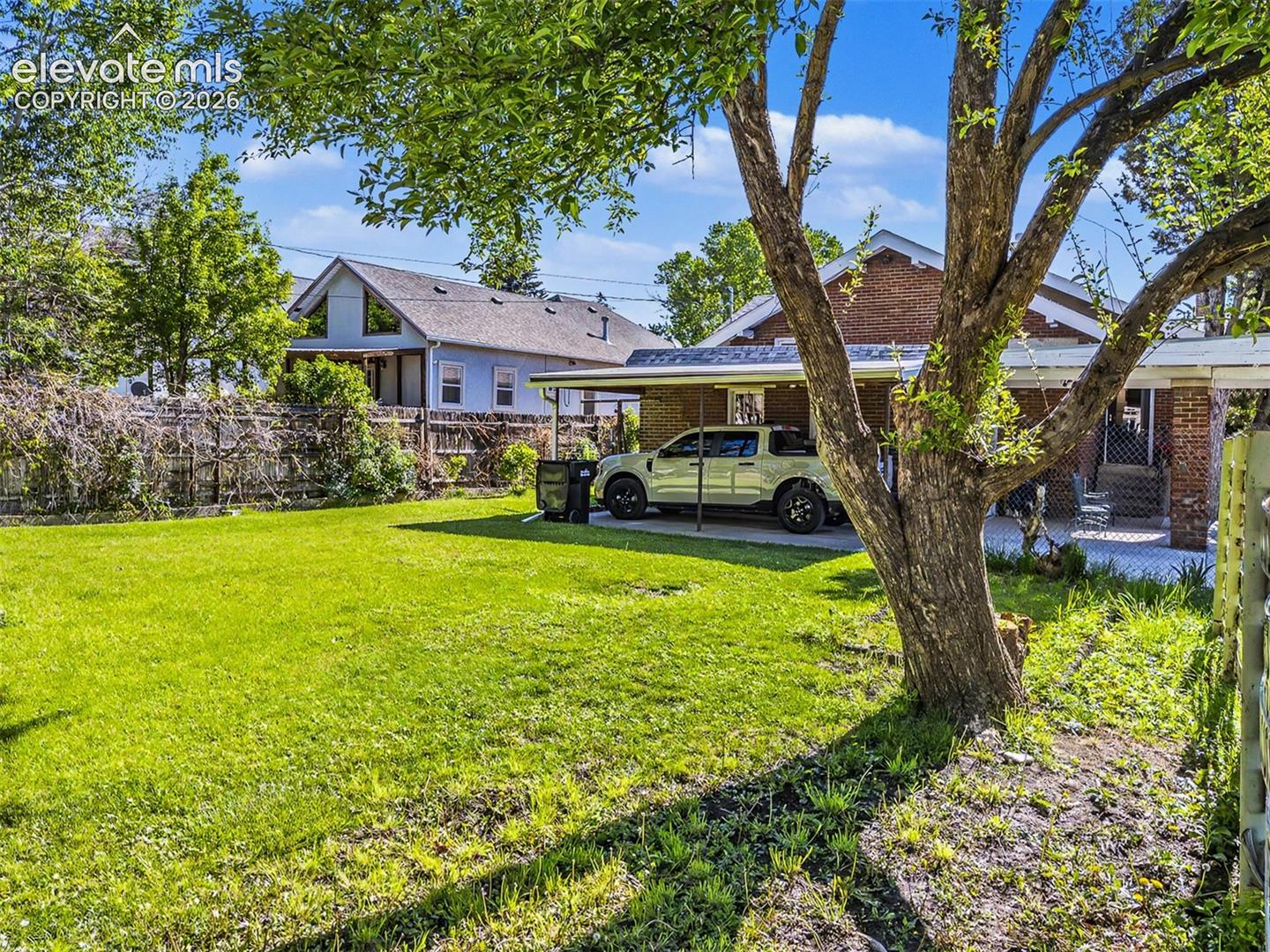 Spacious lawn with a mature tree, featuring a brick exterior and a covered carport with paved surfacing