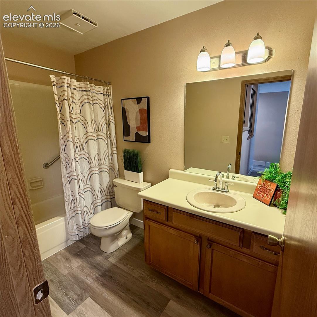 Main level bathroom featuring a wood-finish vanity with a molded countertop and integrated sink, a wall-mounted light fixture with three glass shades, and a wide vanity mirror