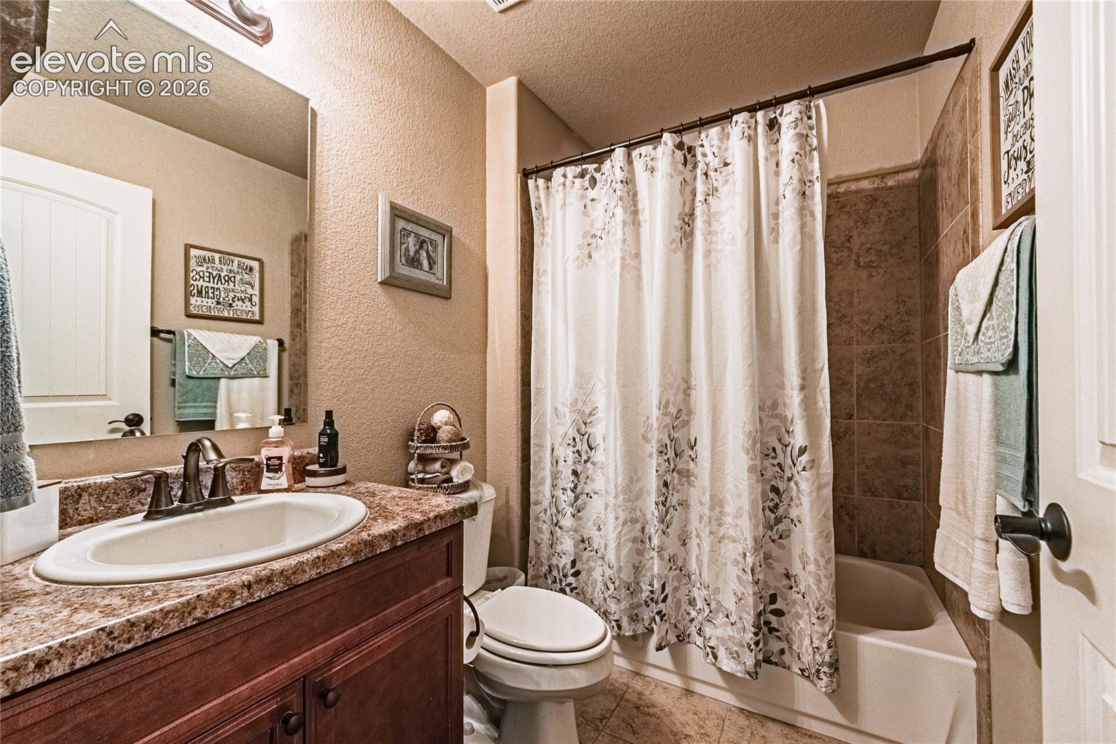 Bathroom with a textured wall, a textured ceiling, shower / tub combo, vanity, and tile patterned floors