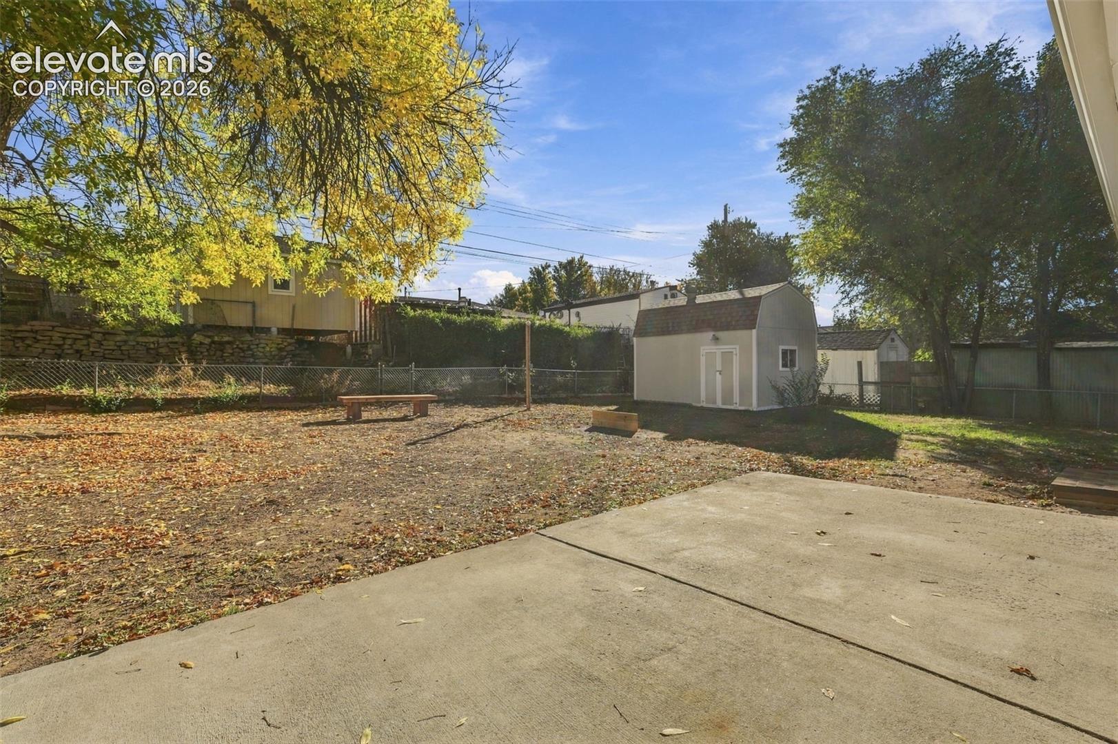 Backyard featuring a concrete patio, detached shed, chain-link fencing, and mature trees