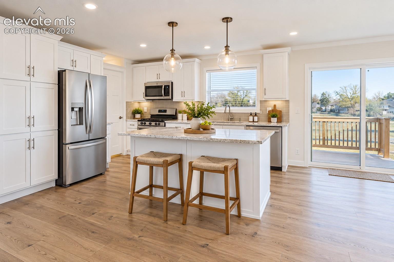 Kitchen – Well-appointed kitchen features a large center island with seating, white shaker-style cabinetry, stainless steel appliances, pendant lighting, and access to the outdoor deck.