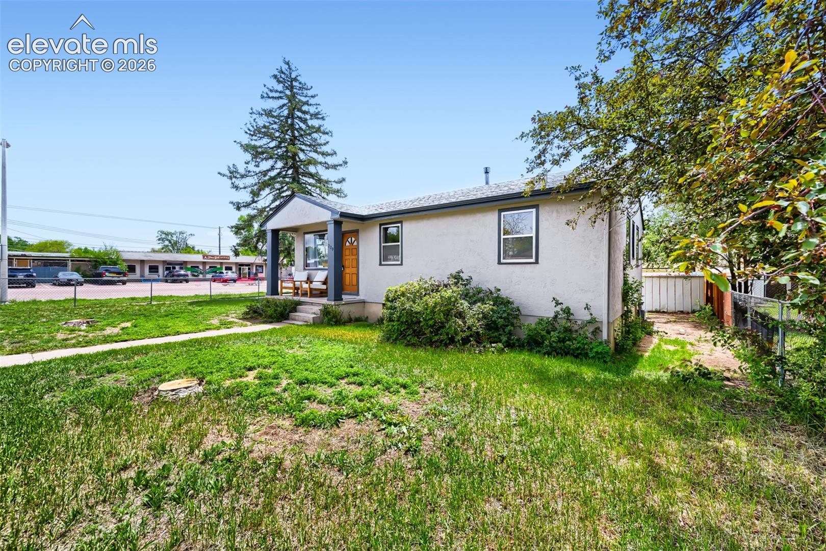Stucco exterior home featuring a covered front porch, an exposed wood front door, and a partially fenced yard