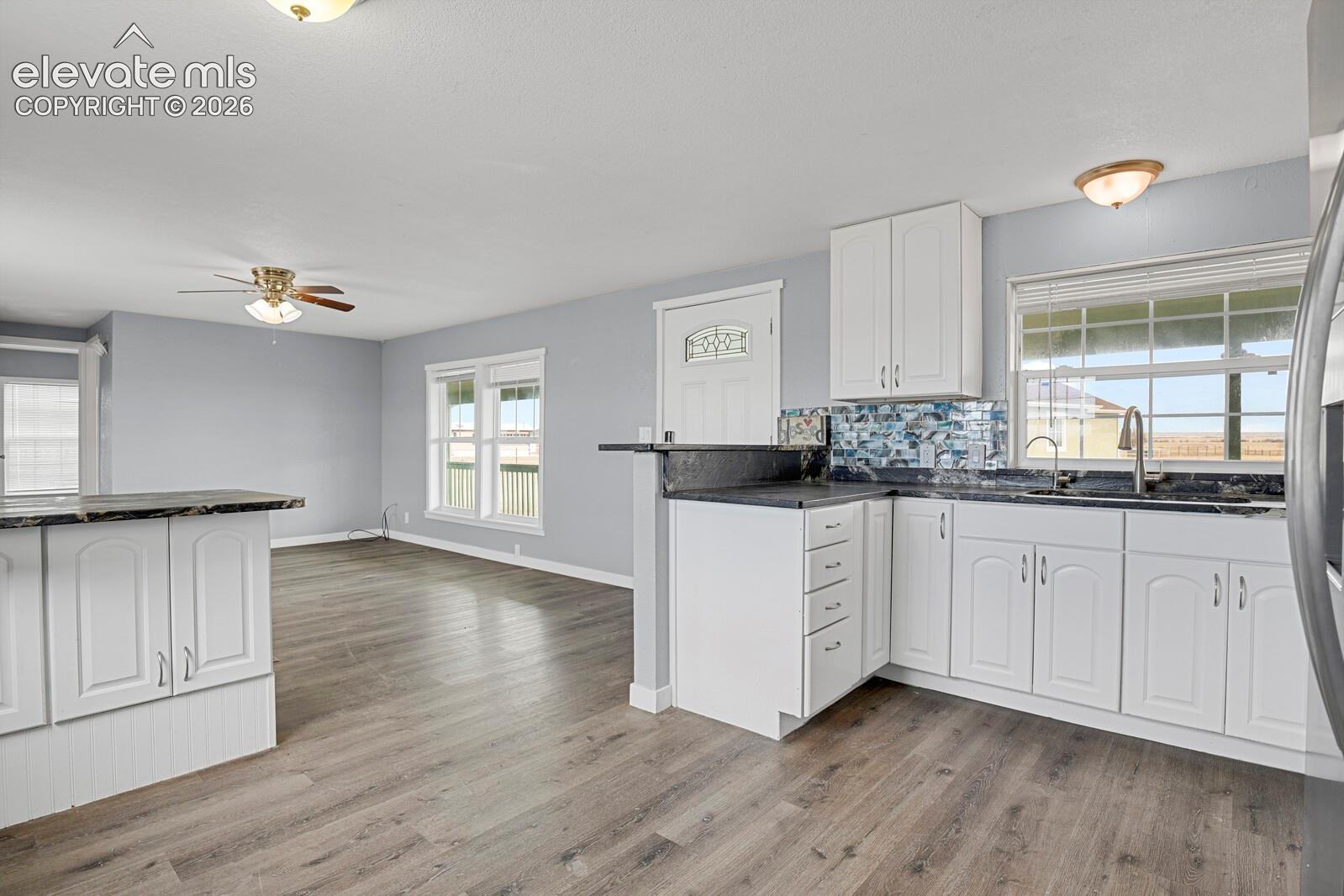 Kitchen featuring white cabinetry, dark countertops, a decorative mosaic tile backsplash, wood-finish flooring, and a ceiling fan