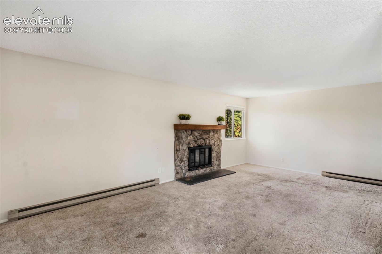 Stone-surround fireplace with a wood mantle, carpet flooring, and a single window