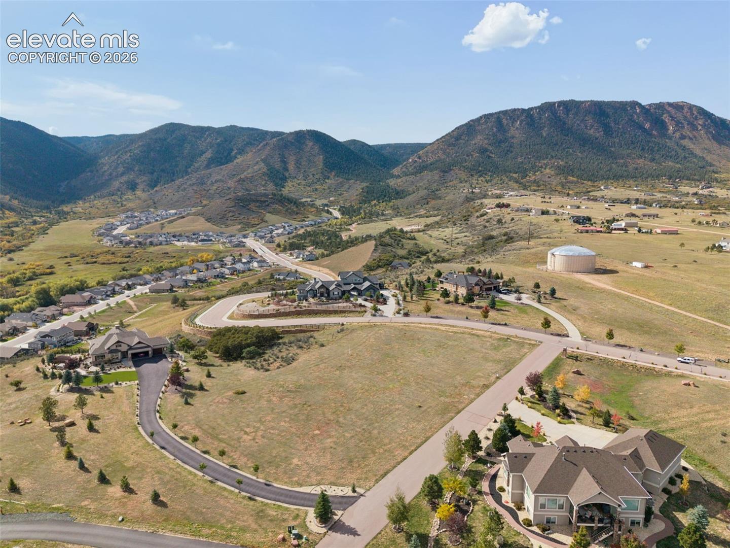 Aerial perspective of rural residential acreage featuring expansive mountain topography, paved access roads, and multiple multi-level dwellings with pitched shingle roofs