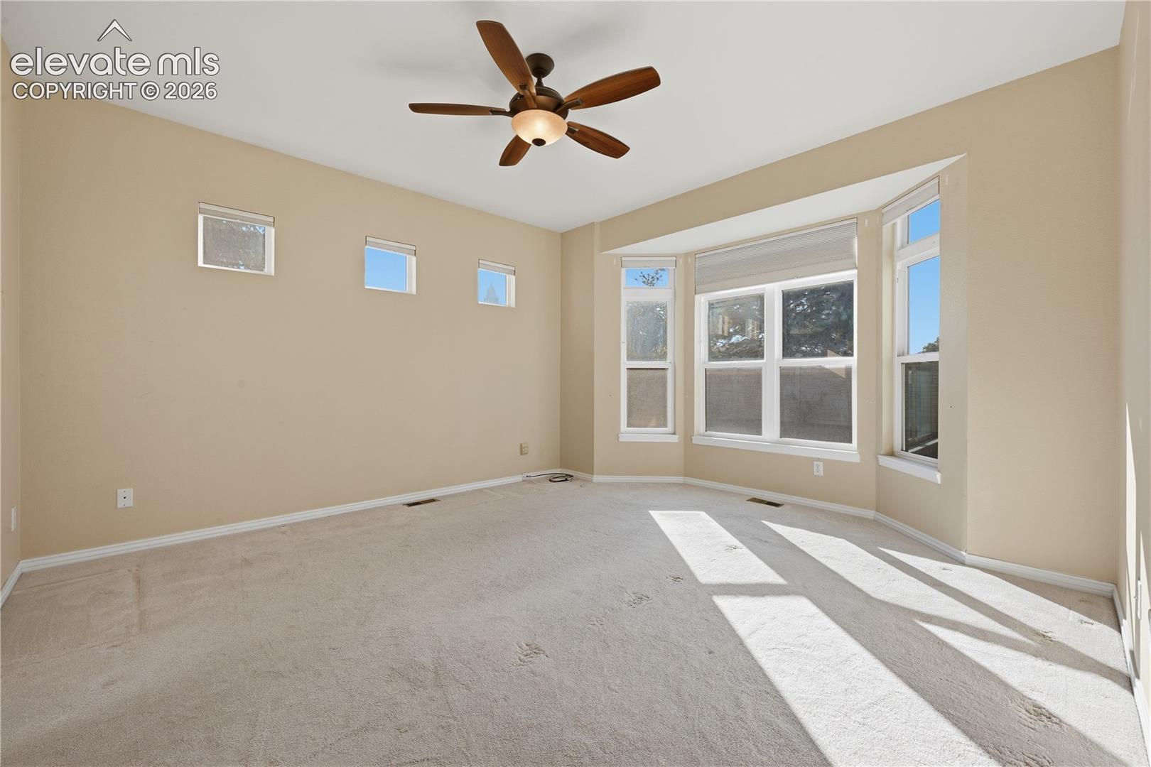 Neutral-toned interior featuring carpeting, a multi-paneled bay window, three clerestory windows, and a ceiling fan with integrated lighting