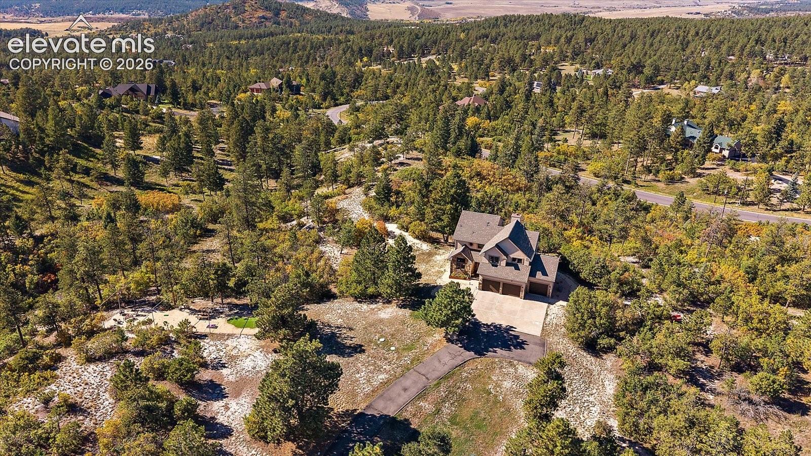 Multi-story residence featuring a paved driveway, multi-car garage, and sprawling grounds surrounded by mature pine forest and mountain terrain
