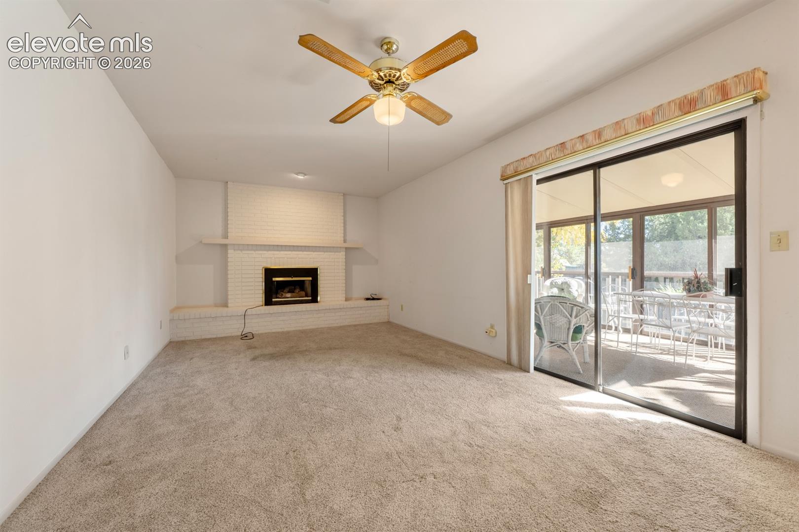 Living space featuring a white brick fireplace with a raised hearth, a ceiling fan with integrated lighting, and a sliding glass door leading to a covered patio
