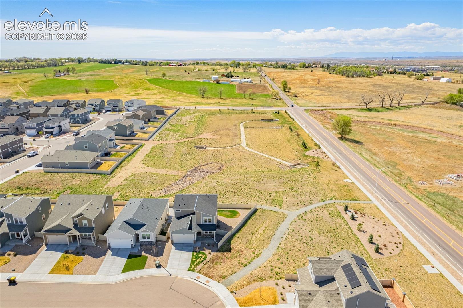 Community setting with diverse housing styles, paved roadways, and undeveloped open land