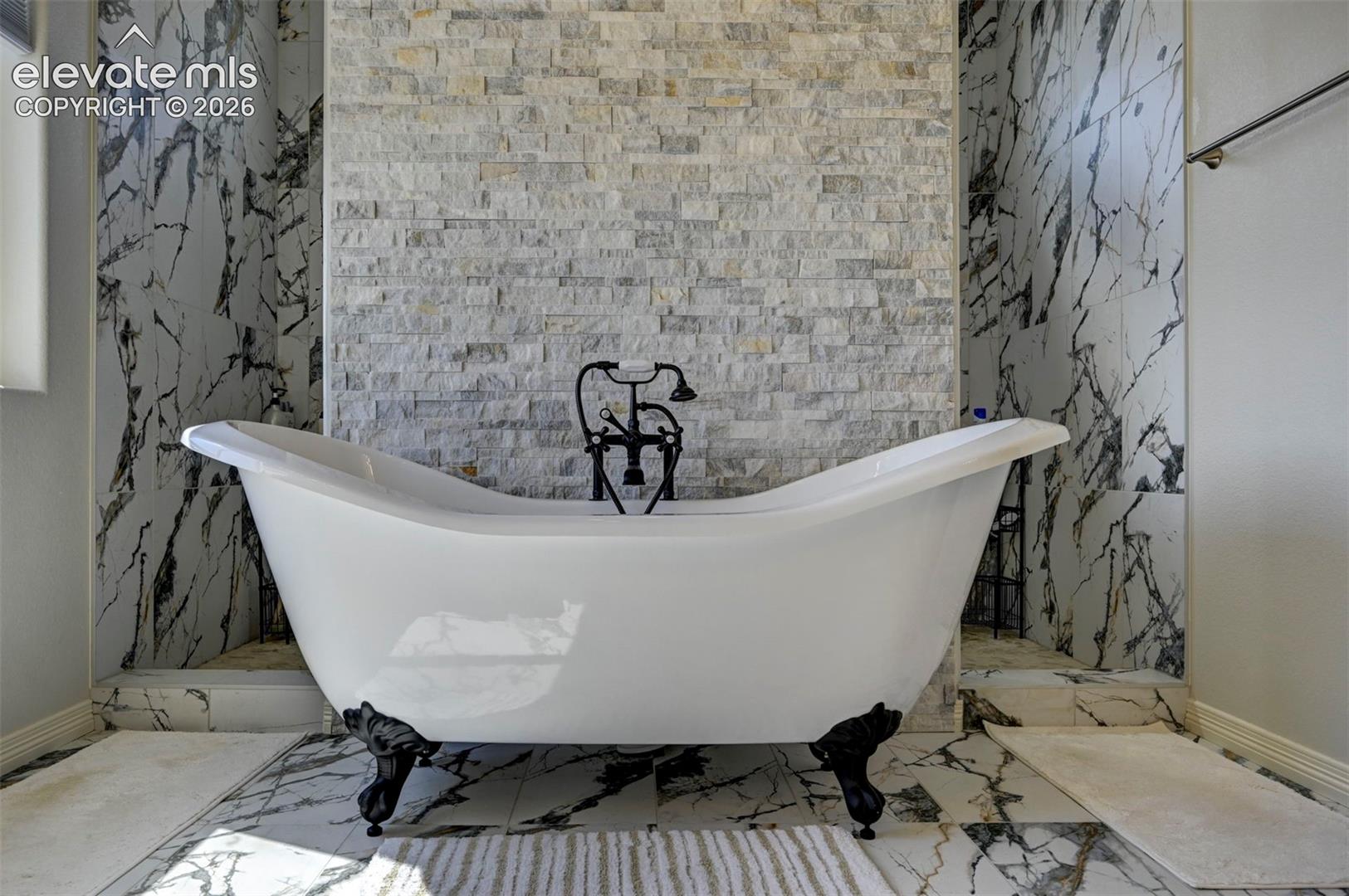 Freestanding clawfoot bathtub with a wall-mounted faucet, set against a stacked stone accent wall