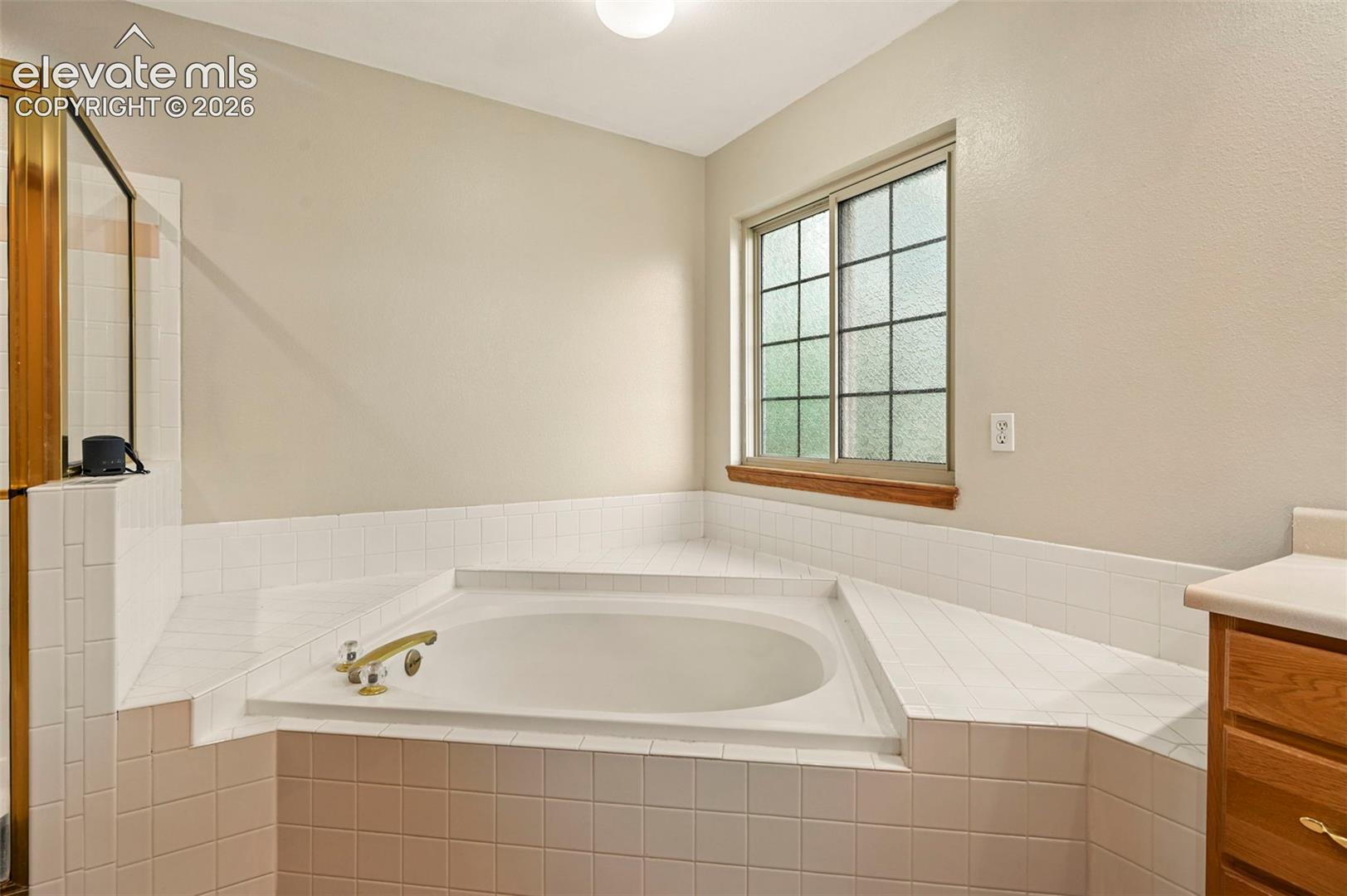 Built-in soaking tub with deck tiling, brass fixtures, and an adjacent shower enclosure