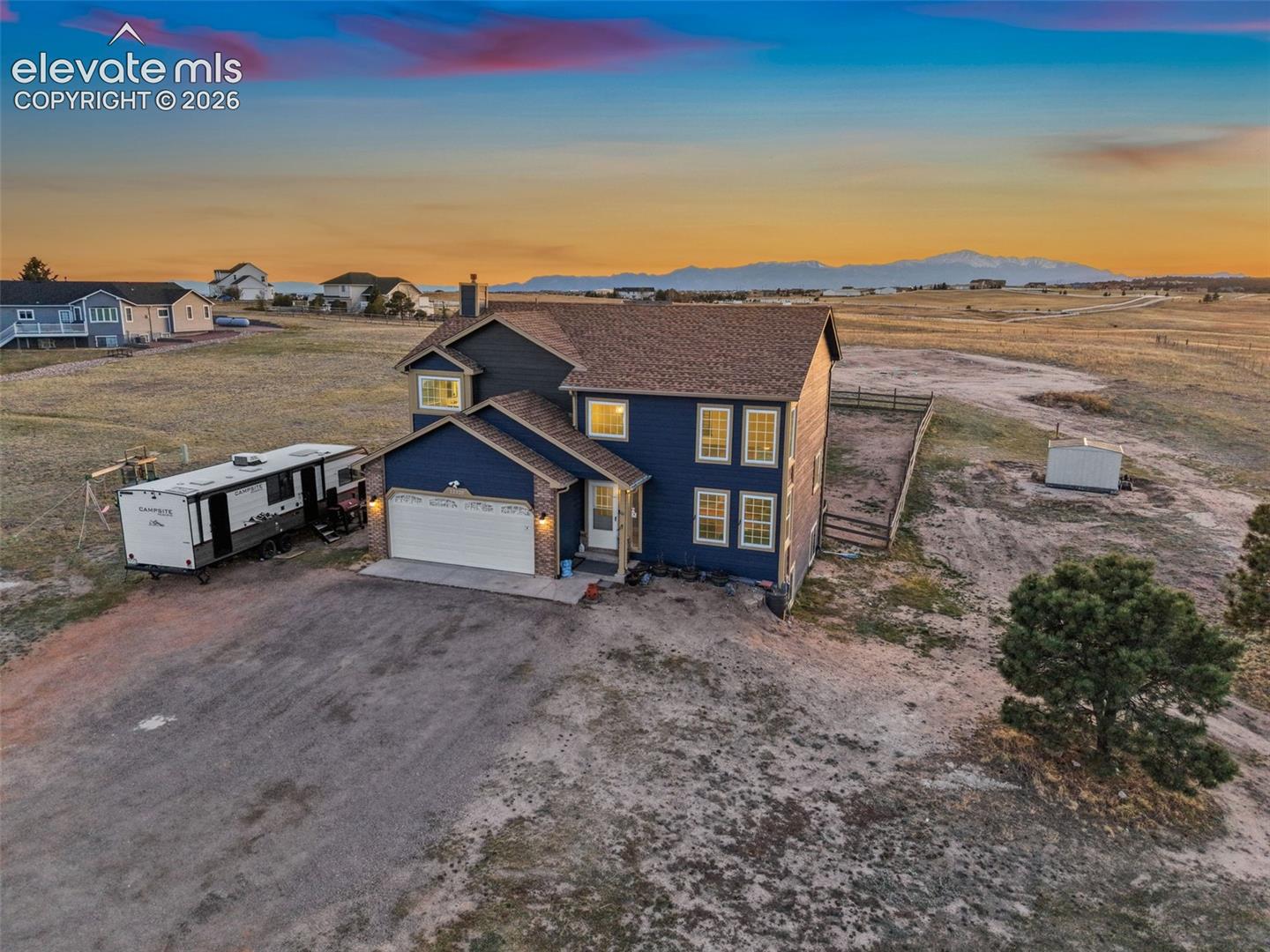 Two-story residence featuring blue siding, a multi-gabled asphalt shingle roof, a two-car attached garage, and mountain horizon backdrop