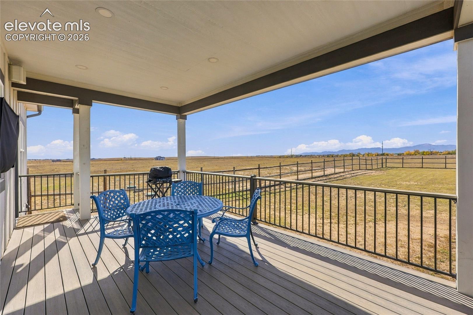 Covered patio featuring composite decking, recessed lighting, and metal railing overlooking a fenced yard with mountain backdrop