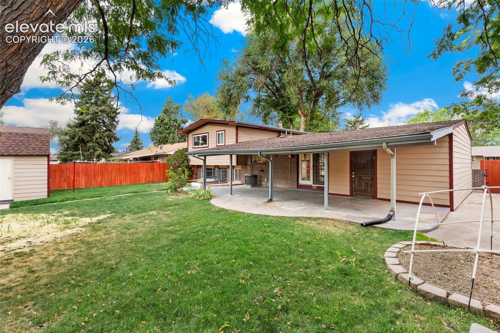 Expansive backyard with a covered patio, manicured lawn, and mature trees