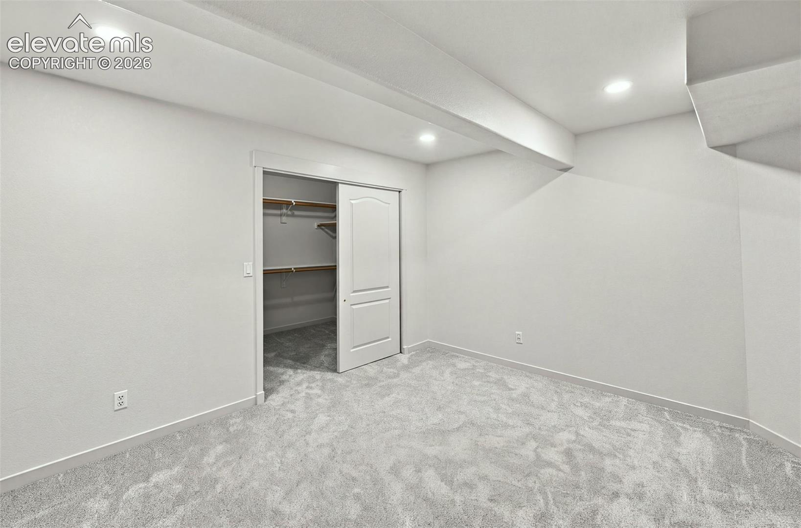 Neutral-toned interior space featuring recessed ceiling lighting, wall-to-wall carpeting, and a closet with sliding panel doors and integrated shelving