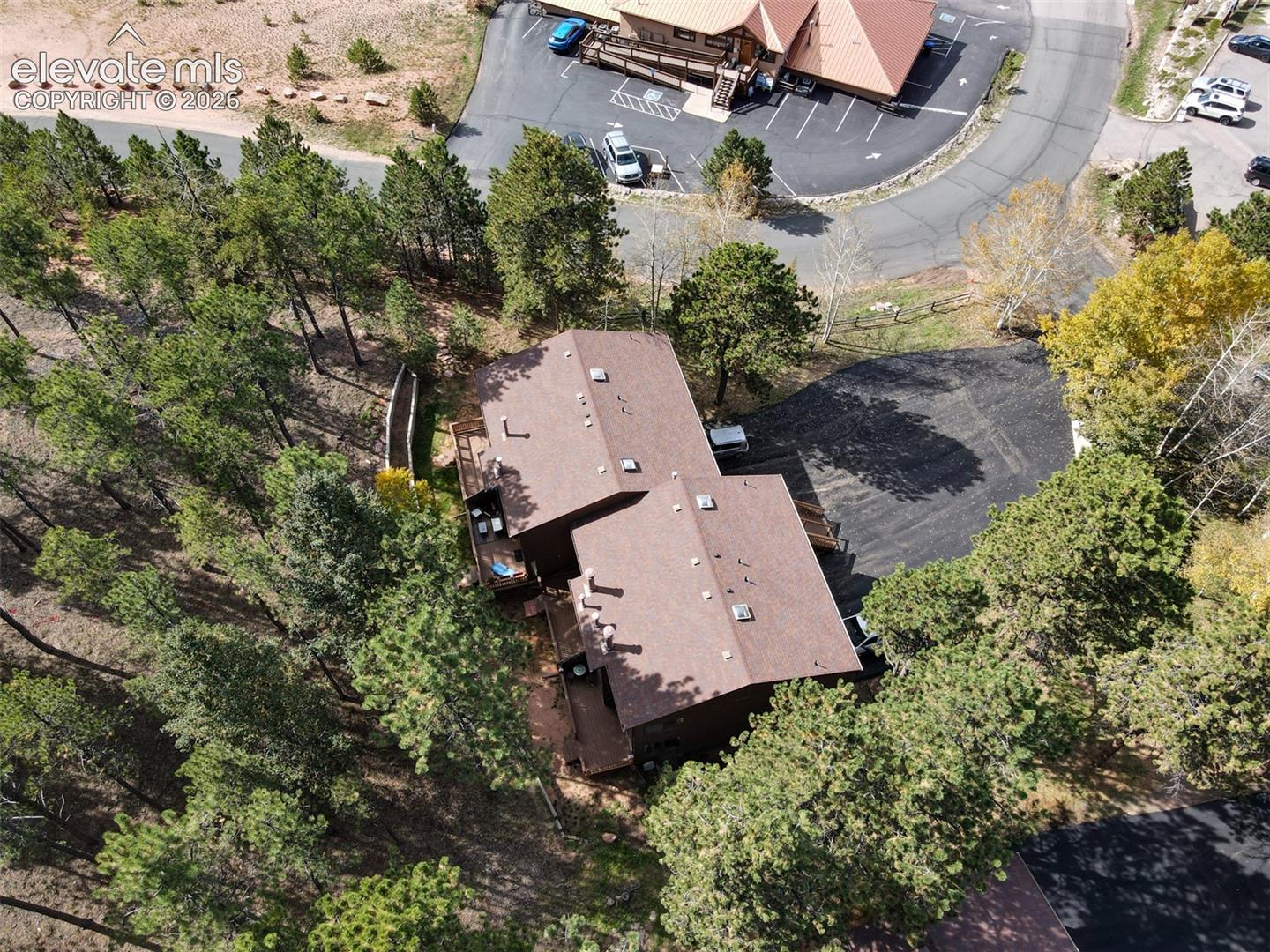 Two-story dwelling with a brown shingle roof, surrounded by mature trees, featuring multiple wood decks