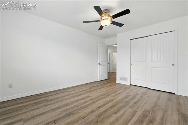 Unfurnished bedroom featuring wood finished floors, baseboards, a closet, and a ceiling fan