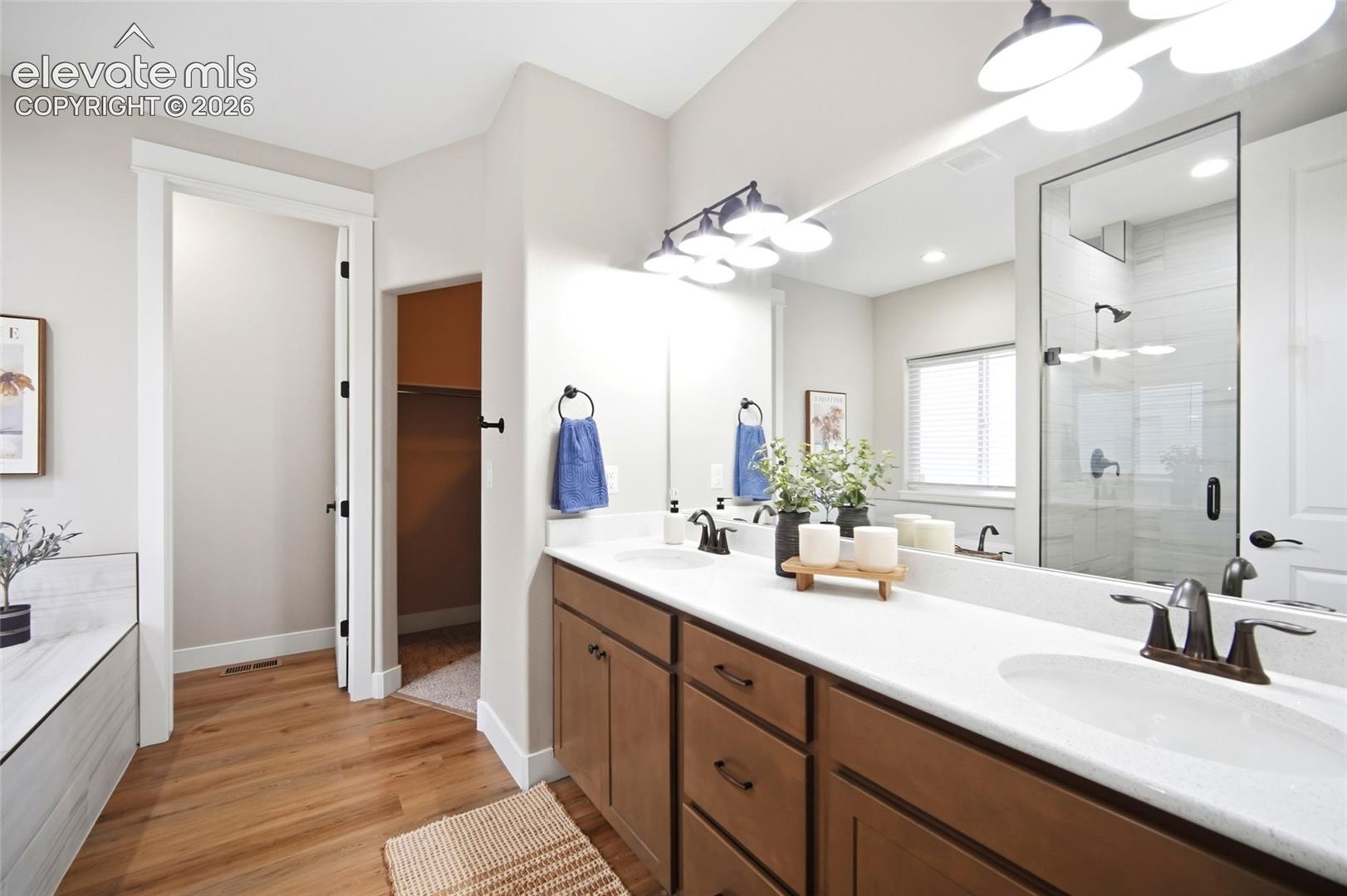 Dual vanity with stone-composite countertop, undermount sinks, matte black fixtures, full-width mirror, and wood-finish flooring