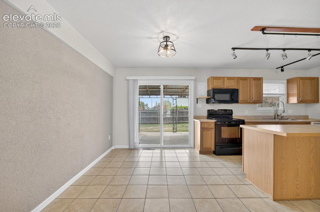 Kitchen featuring wood cabinetry, black appliances, a central island, and tile flooring
